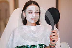 Beautiful woman with white mask on hulf of face. Attractive brunrtte woman in beauty salon