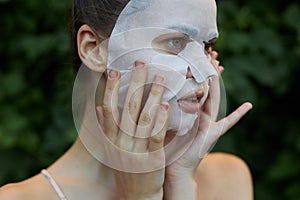 Beautiful woman white mask Look to the side and keep your hands near your face cosmetology bushes in the background