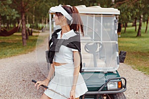 Beautiful woman in white outfit standing near golf cart