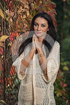 Beautiful woman in white posing in autumnal park. Young brunette woman spending time in autumn near a tree in forest