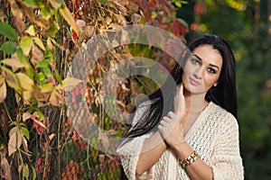 Beautiful woman in white posing in autumnal park. Young brunette woman spending time in autumn near a tree in forest