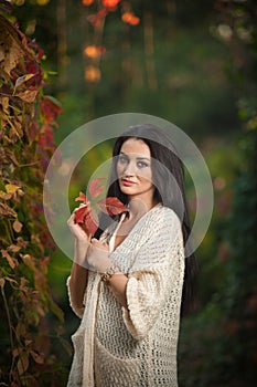 Beautiful woman in white posing in autumnal park. Young brunette woman spending time in autumn near a tree in forest