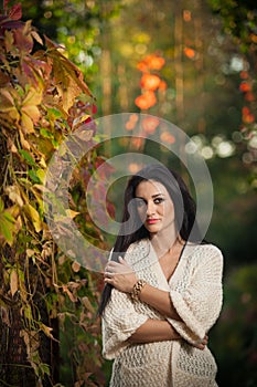 Beautiful woman in white posing in autumnal park. Young brunette woman spending time in autumn near a tree in forest