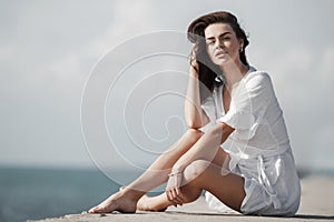 Beautiful woman in white summer dress sitting alone by the sea in summer
