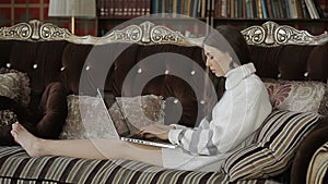 Beautiful woman in white sweater lying on elegant retro sofa with notebook