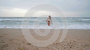 Beautiful woman in the white swimsuit leaves water on the beach during the storm on the sea