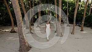 Beautiful woman in white wedding dress is going toward beach through the jungle, tropical island in Maldives