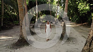 Beautiful woman in white wedding dress is going toward beach through the jungle, tropical island in Maldives