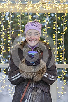 Beautiful woman in winter clothes with coffee in hand On the background of beautiful bokeh. outdoor. vertical photo. Christmas