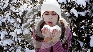 Beautiful woman in winter hat blows off snow from hands