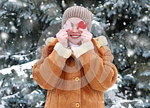 Beautiful woman on winter outdoor posing with heart shape toys, holiday concept, snowy fir trees in forest, long red hair, wearing