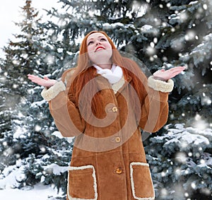 Beautiful woman on winter outdoor, snowy fir trees in forest, long red hair, wearing a sheepskin coat