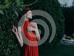 Beautiful woman woman in red dress outdoors near bush luxury charm
