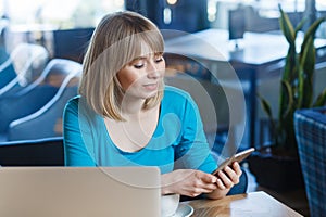 Beautiful woman working on laptop, having break, using cell phone, checking social networks.