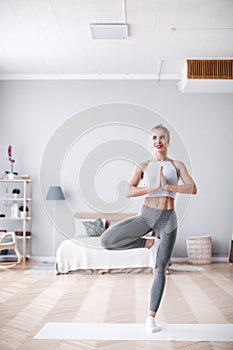 Beautiful woman working out indoors, doing yoga exercise, standing in Vrksasana Posture, Tree Pose, full length