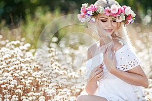 Beautiful woman with a wreath of flowers in summer field