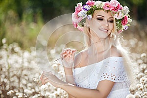 Beautiful woman with a wreath of flowers in summer field