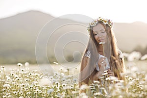 Beautiful woman in a wreath of real flowers, with a bouquet in a field of white daisies