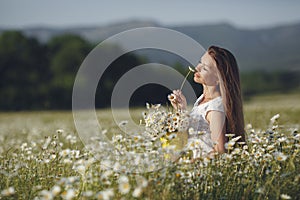 Beautiful woman in a wreath of real flowers, with a bouquet in a field of white daisies