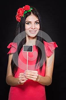 Beautiful woman with a wreath of red flowers holds a wooden plaque