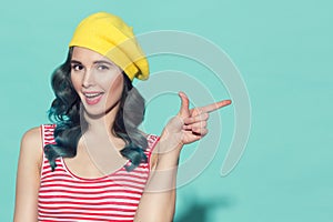 Beautiful woman in a yellow beret pointing finger on copyspace.