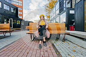 Beautiful woman in yellow beret sits on the street on the bench, depicts emotions. Summer time, yellow colors