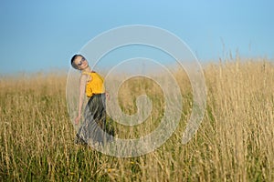 Beautiful woman in yellow shirt and long skirrt standing elegant in beige wheat field. Background of bright blue sky