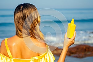 Beautiful woman in a yellow silk dress sprinkles a sun spray on the beach. concept of spf perfect skin red lips bright