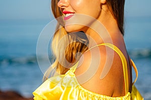Beautiful woman in a yellow silk dress sprinkles a sun spray on the beach. concept of spf perfect skin red lips bright
