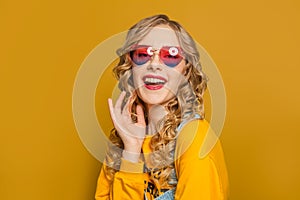 Beautiful woman in yellow sweatshirt and sunglasses on bright background