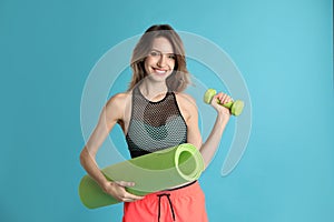 Beautiful woman with yoga mat and dumbbell on turquoise background