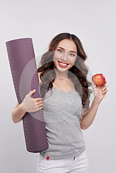 Beautiful woman with a yoga mat, hand holding red apple.