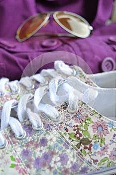 Beautiful womanly shoes with flowers, purple jacket and sunglasses on the background.