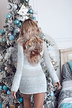 Beautiful women celebrating by Christmas tree. Curly hair. Attractive Blonde girl in dress with long hairstyle enjoyiing in