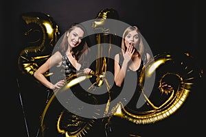 Beautiful Women Celebrating New Year. Happy Gorgeous Girls In Stylish Party Dresses Holding Gold 2019 Balloons