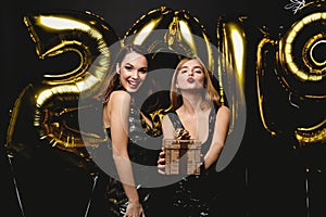 Beautiful Women Celebrating New Year. Happy Gorgeous Girls In Stylish Party Dresses Holding Gold 2019 Balloons