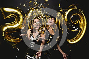 Beautiful Women Celebrating New Year. Happy Gorgeous Girls In Stylish Party Dresses Holding Gold 2019 Balloons