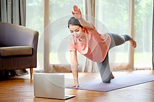 Beautiful women doing yoga by stretching leg and arm and look example from laptop also she look happy and relax. Concept of
