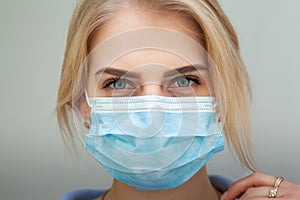 Beautiful Women In A Medical Mask. Blond young woman wearing medical mask adjusting it with her hands close up