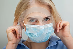 Beautiful Women In A Medical Mask. Blond young woman wearing medical mask adjusting it with her hands close up