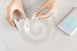 Beautiful women& x27;s hands with up-to-date smartphone and bluetooth headphones on marble background.