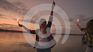 Beautiful women in summer with sparklers dancing in slow motion on the beach at night.