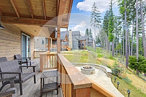 Beautiful wooden back porch with chairs on the hill and large backyard patio with fire pit and pine trees