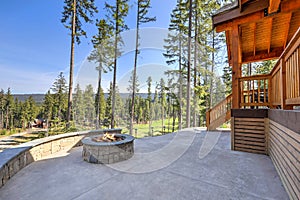 Beautiful wooden back porch with chairs on the hill and large backyard patio with fire pit and pine trees photo