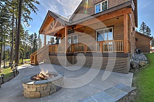 Beautiful wooden back porch with chairs on the hill and large backyard patio with fire pit and pine trees photo