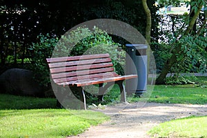 a Beautiful wooden bench stands next to a metal trash can in a park