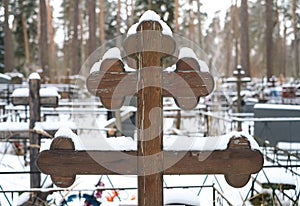 Beautiful wooden cross of traditional shape and artificial flowers on the grave of the Orthodox cemetery in winter.