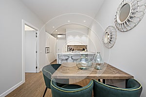 Beautiful wooden dining table with green velvet upholstered chairs, contemporary decor and kitchen island