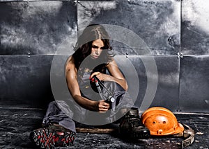 Beautiful worker with a pickaxe and helmet. Seductive and beautiful woman miner sitting on a floor on steel
