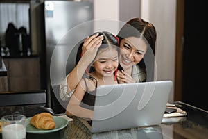 Beautiful working mom using a laptop and spending time with her little daughter at home